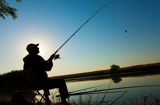 signore che pesca in un laghetto al tramonto. Lui in ombra con una canna da pesca